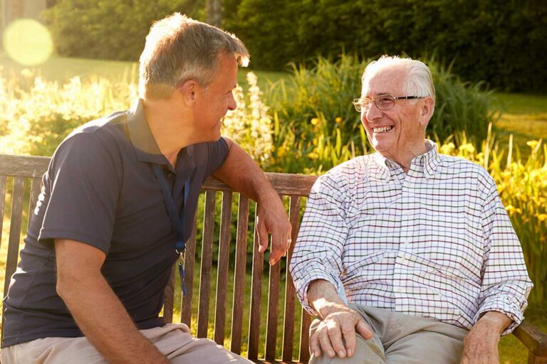Volunteer reads with an older resident in a bright assisted living lounge.
